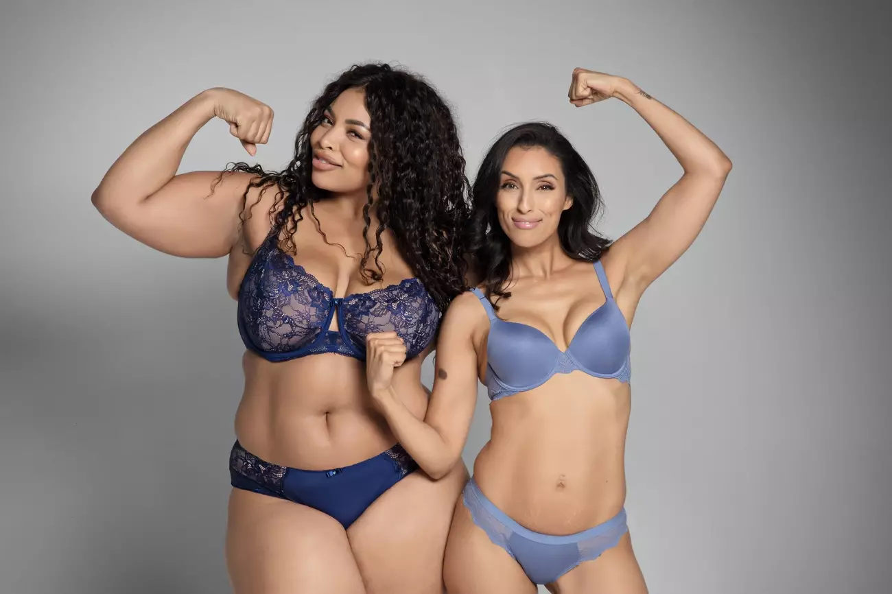 Two women in blue lingerie flex their arms confidently against a gray background in the Parfait Lingerie Perfect Figure Campaign.