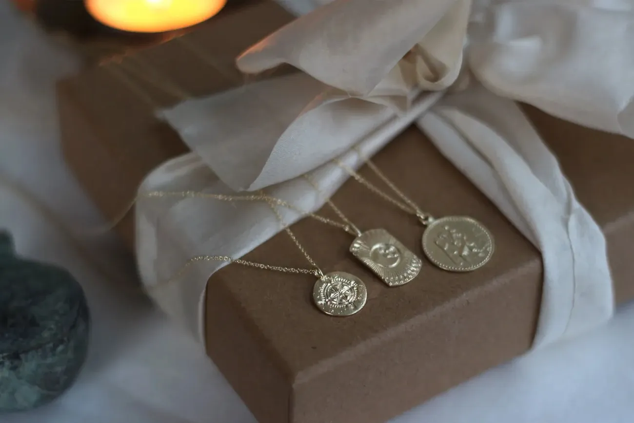 Three gold pendant necklaces displayed on a wrapped gift box with a white fabric bow, evoking a Christmas gift idea.