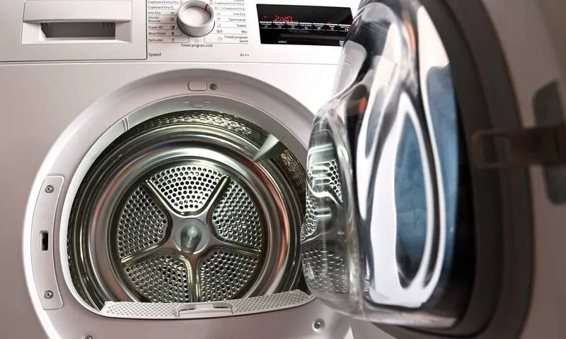 Front-loading white dryer with open door showing stainless steel drum and control panel above