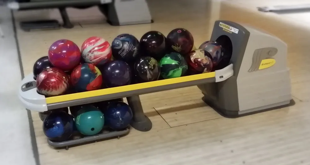 Various colorful bowling balls neatly arranged on a ball return rack at a bowling alley lane.