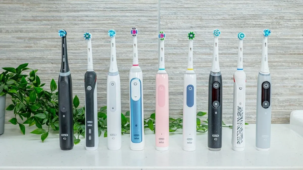 Un alignement de dix modèles différents de brosses à dents électriques Oral-B exposés sur un comptoir, avec une plante en arrière-plan.