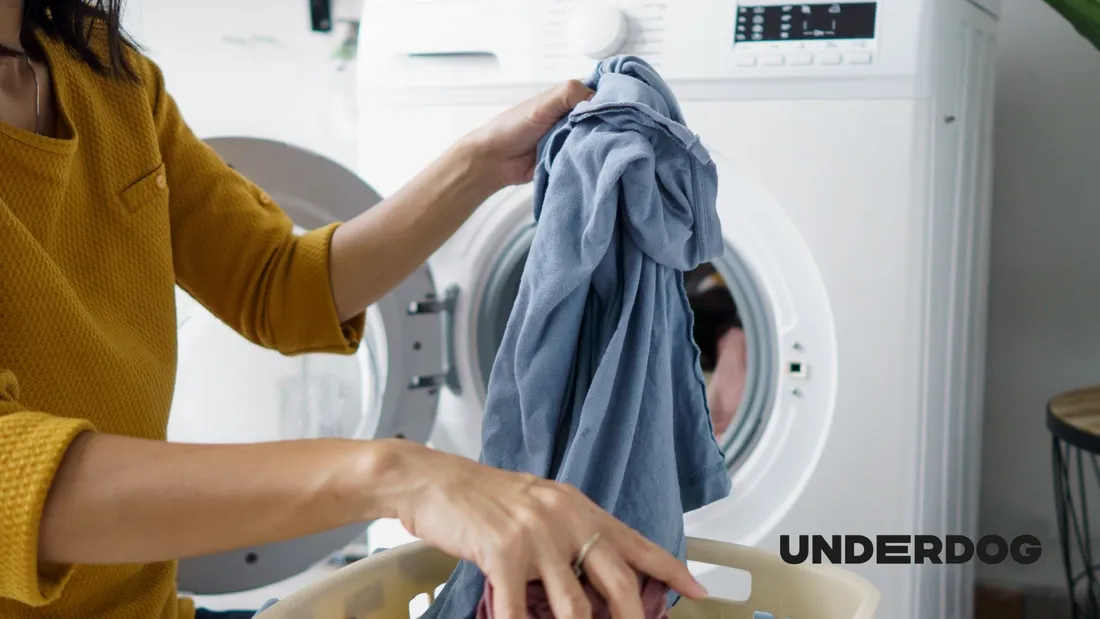 Person removing damp clothes from a front-loading condenser dryer with laundry basket nearby
