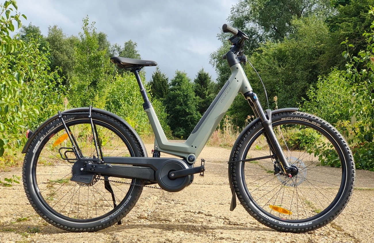 Side view of a Moustache J All Automatic electric bike on a dirt path surrounded by greenery.
