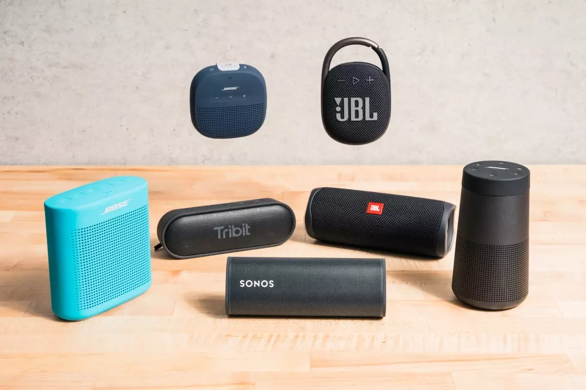 A collection of seven top-rated Bluetooth speakers from brands like Bose, JBL, Tribit, and Sonos displayed on a wooden surface.