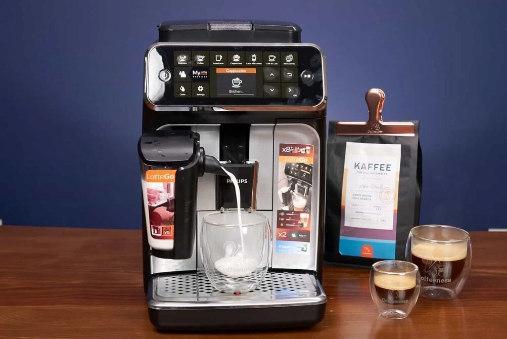 Philips fully automatic coffee machine with milk frother pouring milk into a glass, next to coffee bags and two espresso cups.